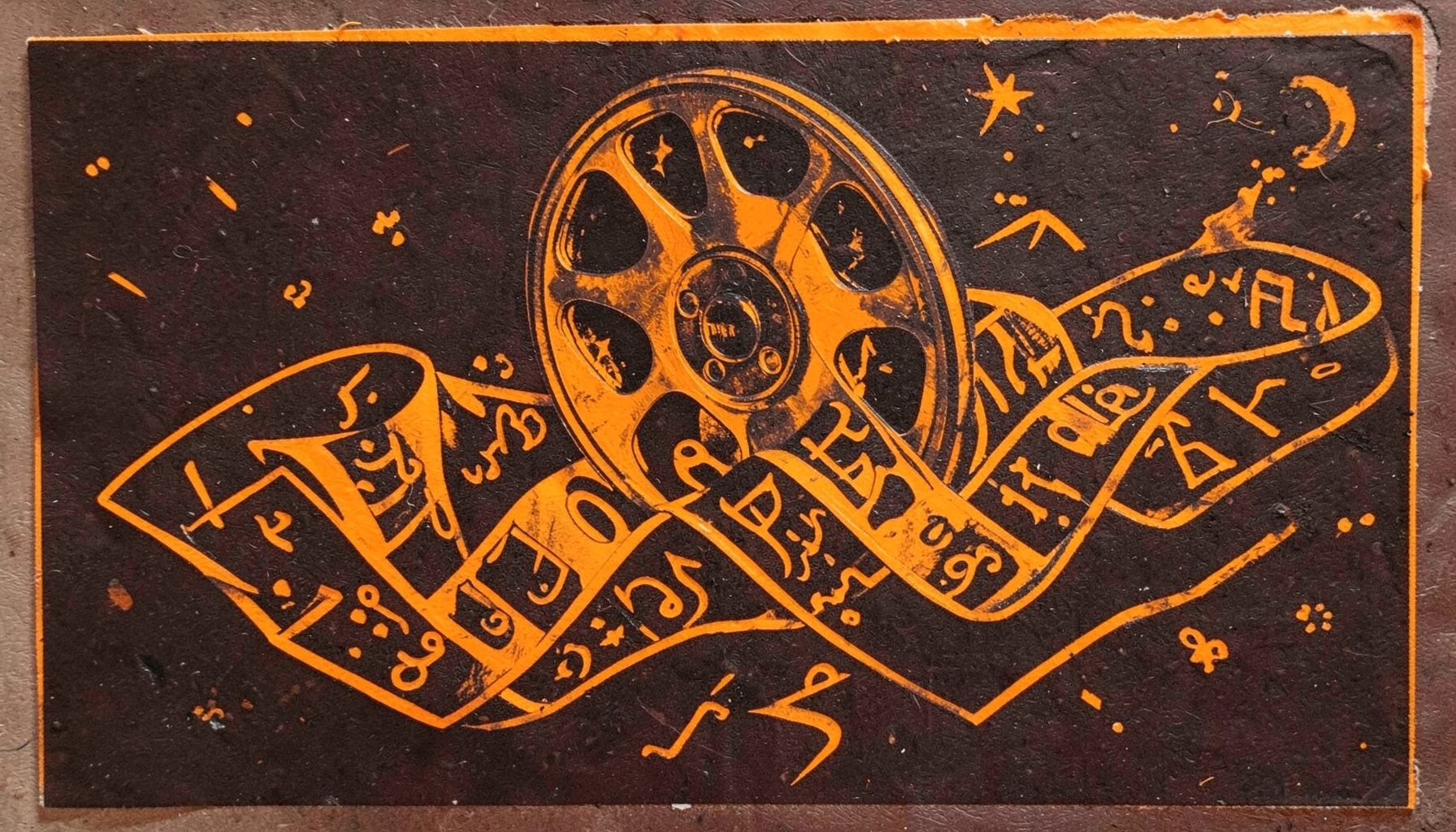 A carved linocut relief print of a film reel unwinding into ribbons that transform into letters of different scripts, warm amber and charcoal tones against a deep brown background