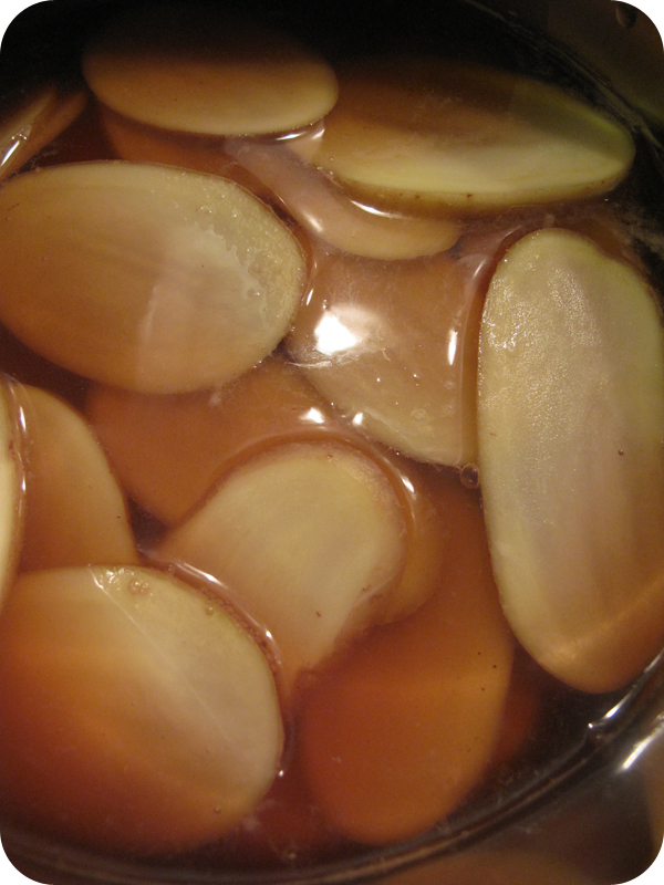 Sliced vegetables simmering in a pot of amber-brown liquid, warm and rich tones