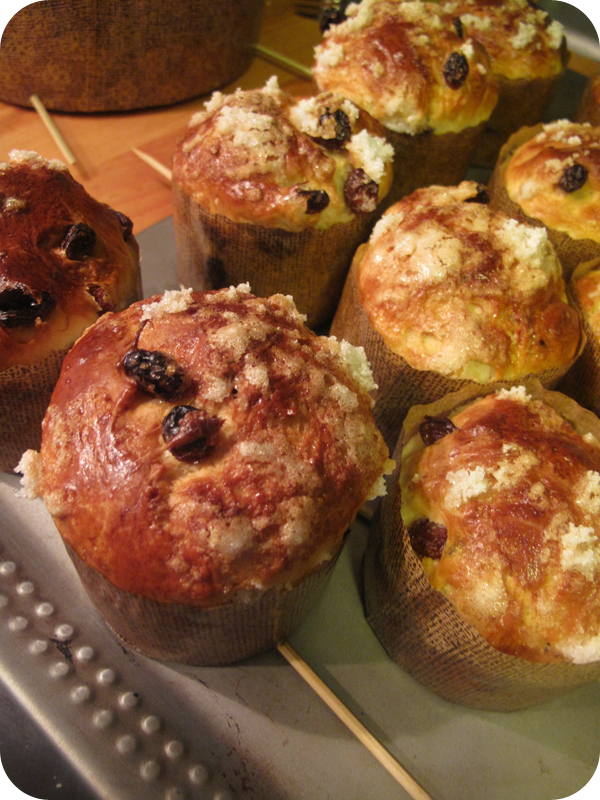Group of baked sweet breads with sugar topping and dried fruit arranged on a tray, warm brown and gold tones